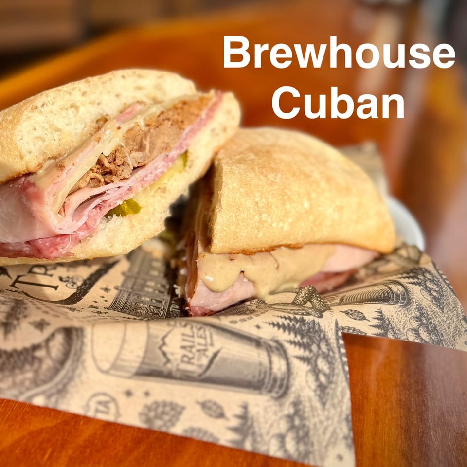 Two Cuban sandwiches with ham, pork, Swiss cheese, pickles, and mustard on a newspaper-lined plate.