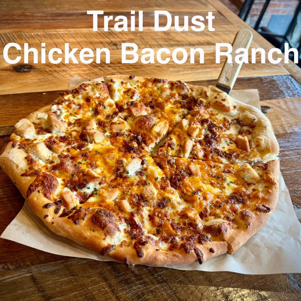 Chicken bacon ranch pizza topped with melted cheese, diced chicken, bacon, and herbs on a wooden restaurant table.