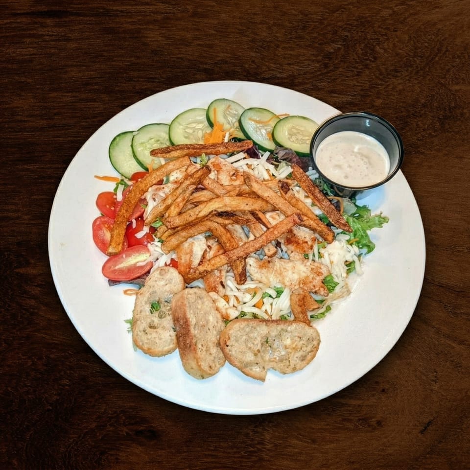 A white plate with a salad topped with chicken, fries, cucumbers, tomatoes, and garlic bread.
