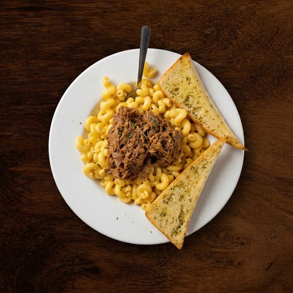 Macaroni and cheese topped with pulled pork and two slices of garlic bread on a white plate.