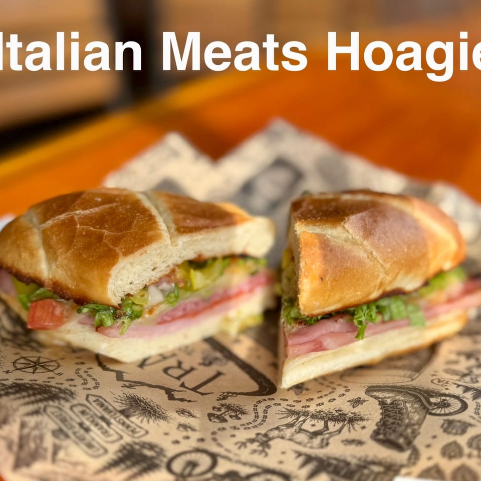 Two Italian meat hoagies with deli meat, lettuce, and tomatoes on map-printed deli paper.