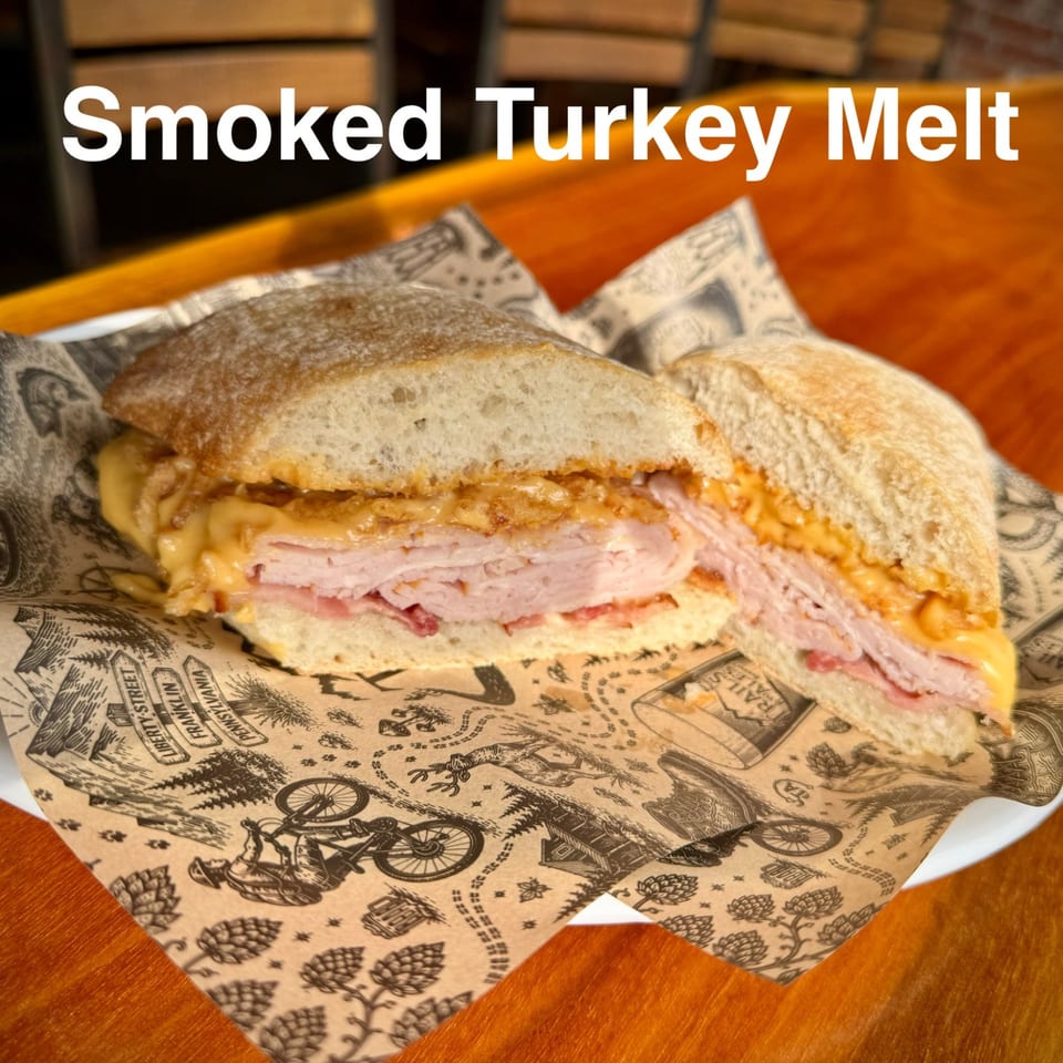 Smoked turkey melt with sliced turkey, melted cheese, and sauce on toasted bread, served on patterned paper over a wooden table.