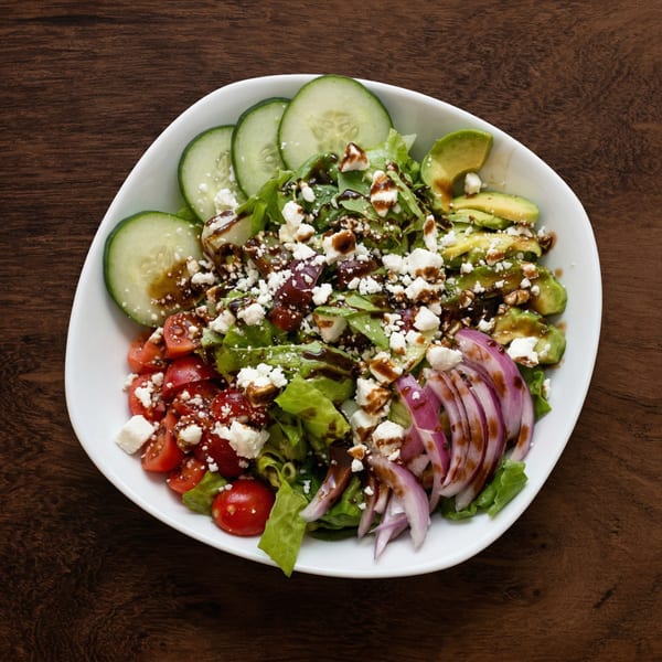 A fresh salad with lettuce, tomatoes, cucumbers, avocado, red onion, feta, and balsamic glaze.