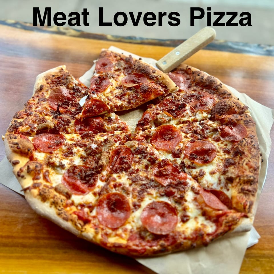 Meat lovers pizza topped with pepperoni, ground meat, and melted cheese on a wooden table.